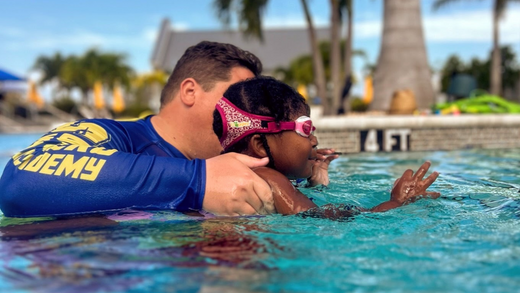 Toddler girl in mermaid swimsuit and Frogglez swim goggles taking swim lessons from swim teacher instructor. Best goggles for girls swim lessons. kids swim goggles. goggles. best kinds swim goggles. kids swim. swim instructor. frogglez. swim goggles. 