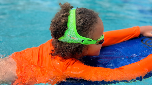 Boy wearing green Frogglez swimming goggles using kick board at swim lessons 
