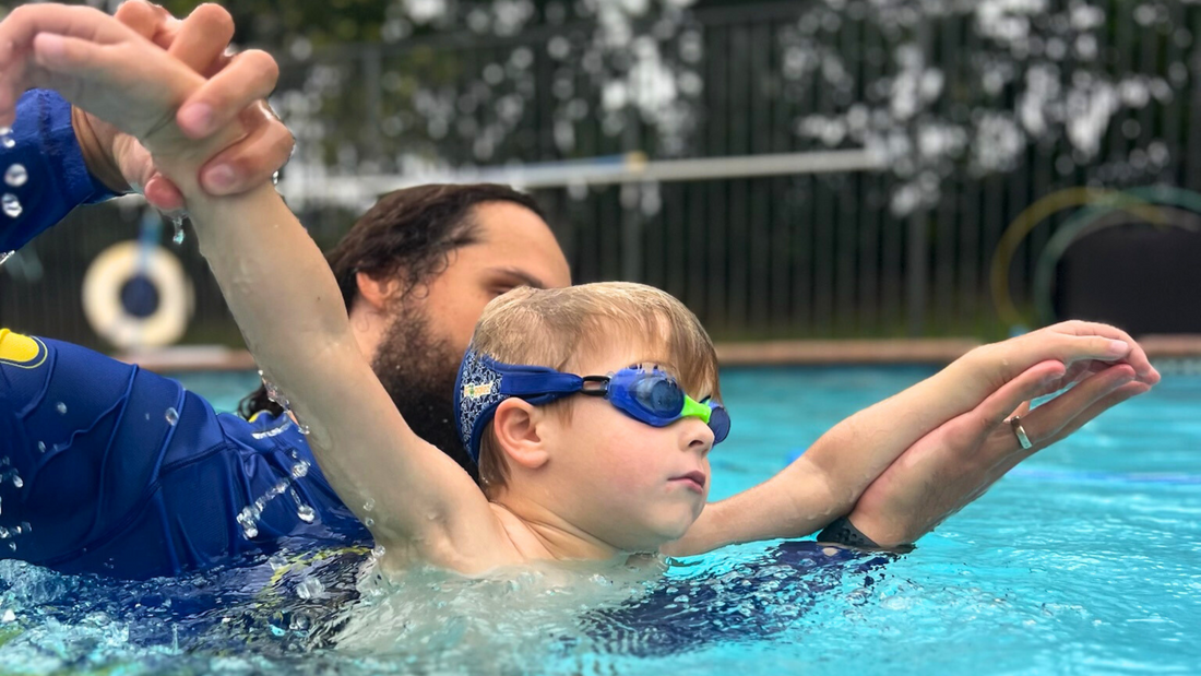 Child learning how to swim with swim instructor during lessons. Wearing Blue Frog Frogglez Goggles, Certified Autism Resources, Kids Water Gear