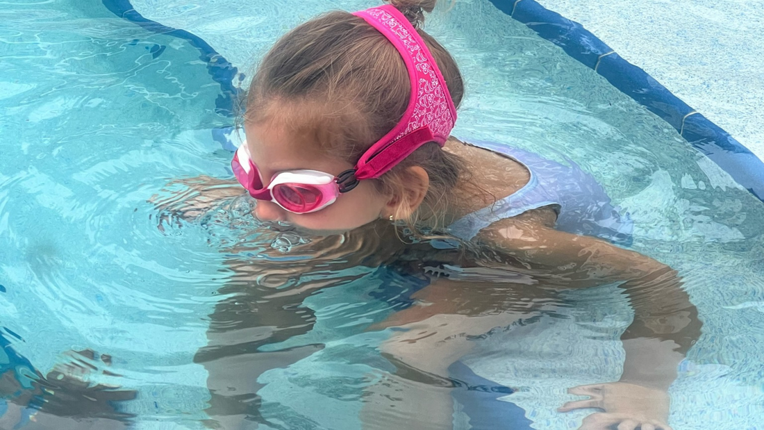 Child swearing Frogglez Goggles Swim Goggles pink frogz with her face in pool practicing blowing bubbles. tips for toddlers before starting swim lessons